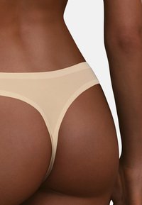 String nu avec une finition lisse et transparente et une taille contrastante. Présente un design minimaliste, épousant les courbes avec des bords sans coutures.