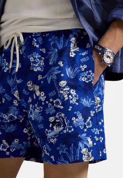 Bañador azul con un estampado floral y de osos, que cuenta con una cintura con cordón y una tela texturizada. Se lleva un reloj en la muñeca.