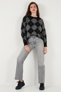 Maglione argyle nero e grigio con maniche lunghe, abbinato a jeans grigi a vita alta e sneakers nere, su uno sfondo uniforme.