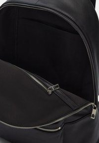 Zaino in pelle nera con finitura liscia, dotato di un ampio interno foderato in tessuto nero, doppi scomparti con zip e dettagli in metallo argentato.