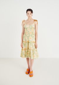Bloemige jurk in lichtgeel met groene en oranje details, met een smock-bustier, een gelaagde rok en verstelbare bandjes.