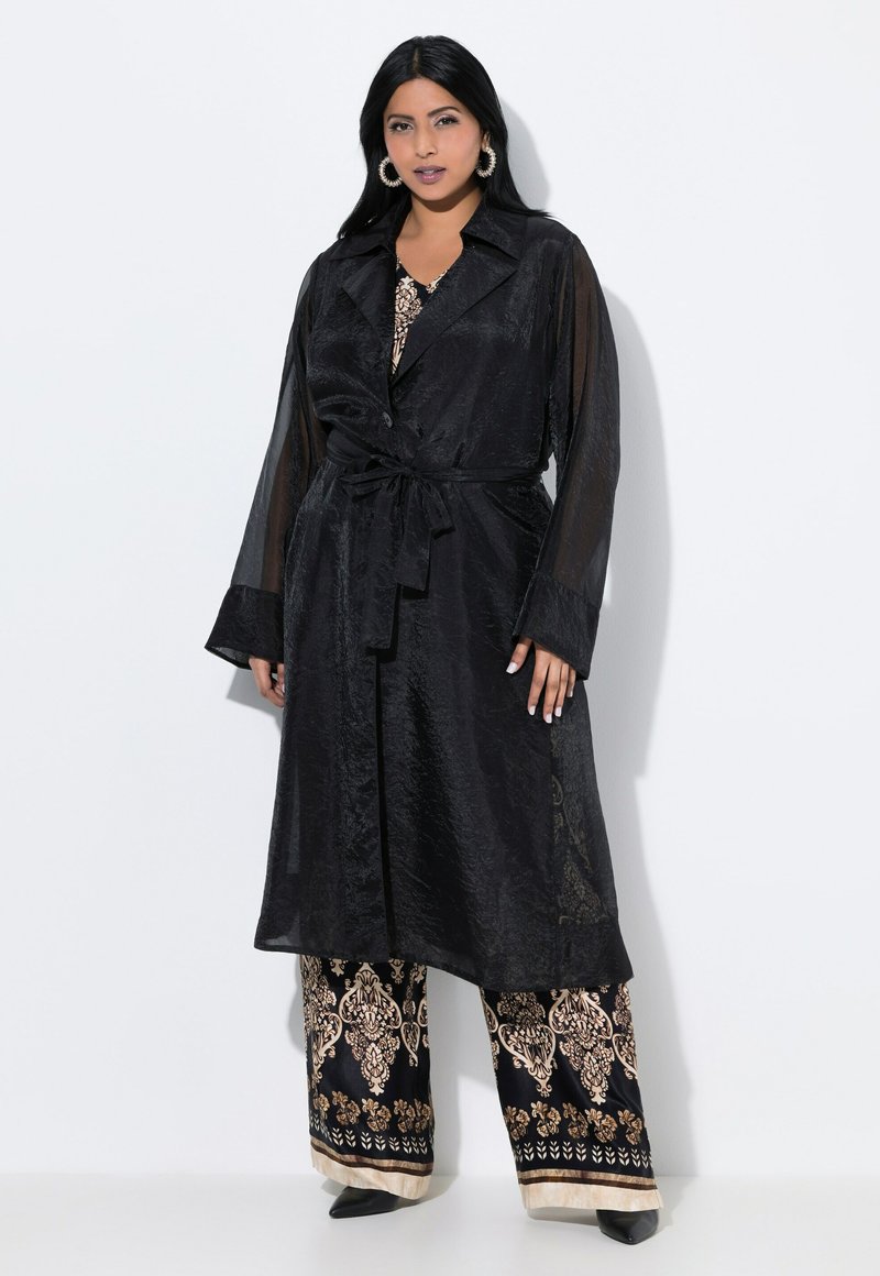 Black long coat with a tie waist and transparent sleeves, paired with wide-legged pants featuring a gold floral pattern and black trim.
