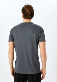 Grijs sportshirt met korte mouwen van gestructureerde stof. Heeft een ronde halslijn en een subtiele logo op de bovenrug.