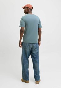 Light blue short-sleeve shirt paired with loose-fitting blue jeans and tan footwear, complemented by a soft orange cap.