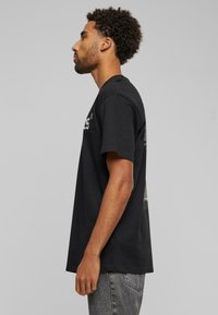 Sort bomulds T-shirt med korte ærmer, rund halsudskæring og et grafisk design på ryggen. Løs pasform med en blød tekstur.