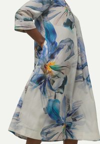 Vestido floral con grandes flores azules y moradas sobre un fondo claro, con mangas 3/4 y un diseño fluido hasta la rodilla.