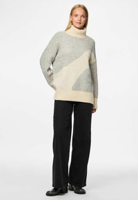 Hele hallitusrohelise ja kreemika lõngaga kootud sviiter, millel on kõrge kaelus ja geomeetrilised mustrid. Kanda mustade laiad püksid ja mustad pahkluu saapad.