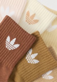 Sett med fem par strikkede sokker i pastellfarger (rosa, gul, brun) med hvit logo av trebladdesign og ribbestruktur.