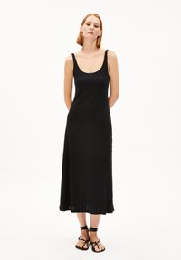 Black sleeveless midi dress with a scoop neckline, ribbed texture, and a flowing silhouette, paired with black strappy sandals.