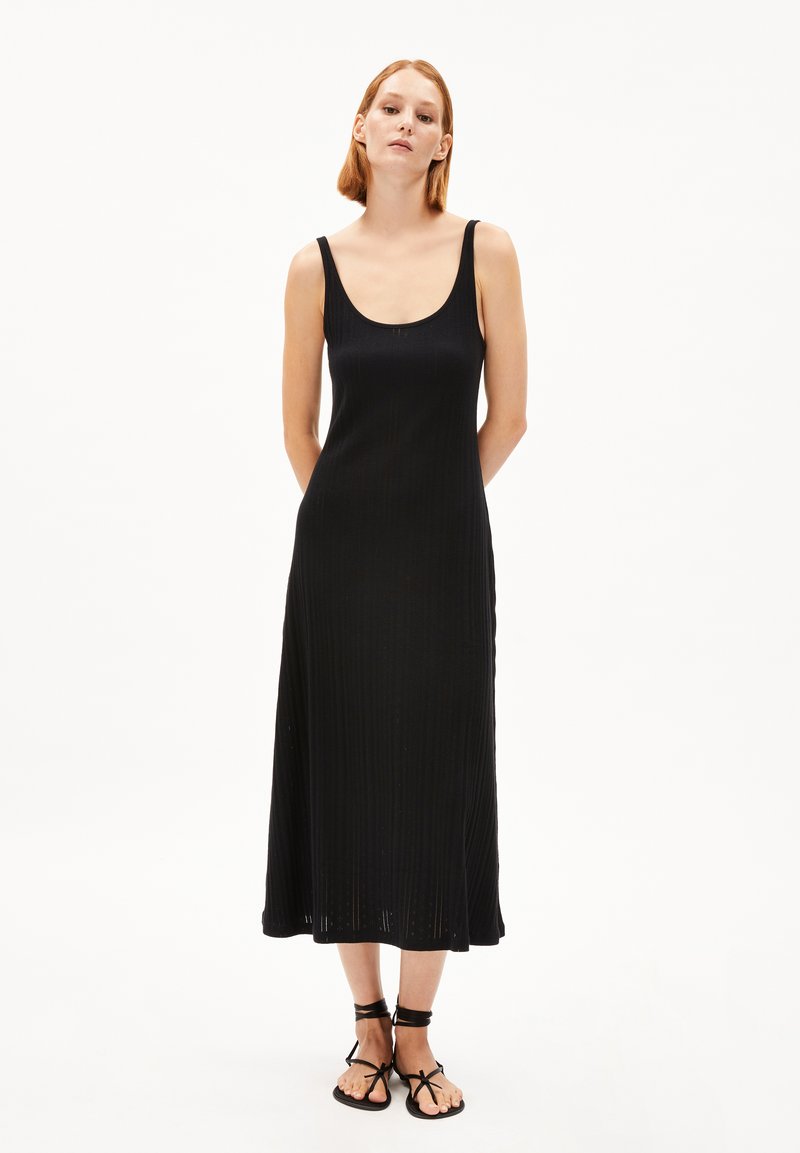 Black sleeveless midi dress with a scoop neckline, ribbed texture, and a flowing silhouette, paired with black strappy sandals.