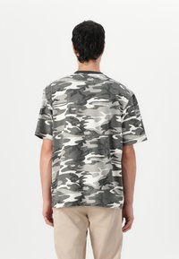 Kortermet t-skjorte i grå camo med hvite detaljer, laget av mykt stoff; har rund hals og avslappet passform.