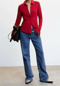 Chemise rouge à manches longues avec un col et des poignets évasés, associée à un jean en denim léger bleu clair, ample, et des chaussures argentées à bout pointu.