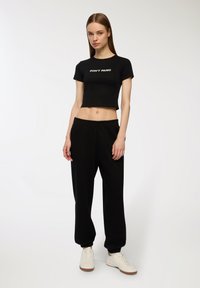 Maglietta nera cropped con testo bianco "NON ENTRARE IN PANICO", abbinata a pantaloni della tuta neri comodi e scarpe bianche. Tessuto morbido, vestibilità rilassata.