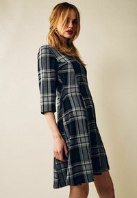 Musta ja harmaa ruudullinen mekko, jossa on kolme neljäsosapituista hihaa, A-linjainen muotoilu, teksturoitu kangas, keskipitkä pituus ja hillityt saumat.