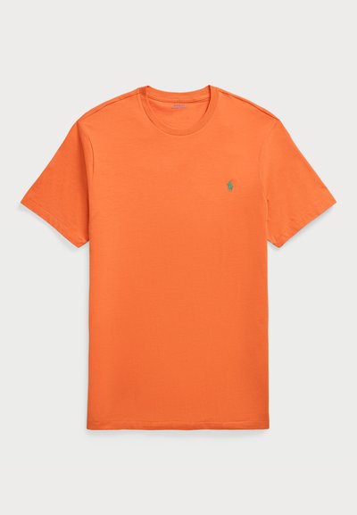 Πορτοκαλί βαμβακερό T-shirt με κοντά μανίκια, στρογγυλή λαιμόκοψη και ένα μικρό πράσινο κεντητό λογότυπο στο αριστερό στήθος. Απαλή υφή.