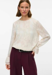 Helebeež blouse lillemustriga, pikad varrukad volangidega, kombineeritud sügava burgundi värvi kõrge vöökohaga pükstega ja musta vööga.