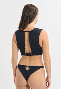 Ensemble de bikini noir comprenant un haut court avec un dos lacé et des accents circulaires. Le bas a un design à couverture minimale.
