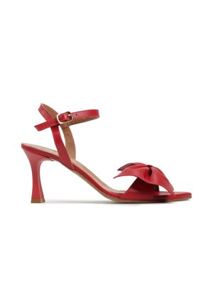 Czerwona sandałka na średnim obcasie z paskiem wokół kostki i klamrą, ozdobiona dużą dekoracyjną kokardą na pasku przy palcach.