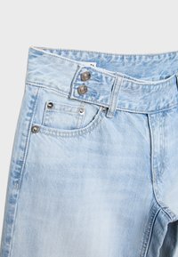 Lyseblå denimjeans med dobbelt knaplukning, forlommer med metalnitter og synlige bæltestropper på en ensfarvet baggrund.