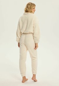 Kremowy, puszysty zestaw dresowy z polaru, zawierający krótki top z kołnierzykiem oraz spodnie z elastycznym paskiem w kostkach.