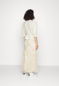 Blommig blus i ljusgult och grått med puffärmar, i kombination med en tvålagers krämfärgad kjol med rutigt mönster och volangkanter.