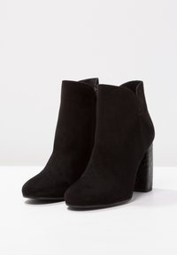 Czarne zamszowe botki za kostkę z wysmuklonym noskiem i fakturowanym obcasem w kształcie kostki. Zamek błyskawiczny z boku ułatwia zakładanie, a gładkie wykończenie z subtelnymi detalami przeszycia.