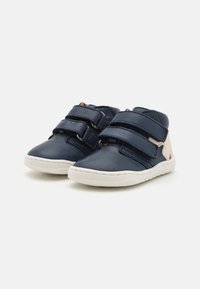 Marineblaue Leder-Schuhchen für Kleinkinder mit zwei Klettverschlüssen, weiße Sohle und beigen Akzenten an der Ferse. Runder Zehenbereich und flexibles Design.
