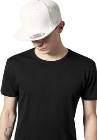 Fehér snapback sapka lapos karimával, gyapjú anyag; fekete rövid ujjú galléros pólóval párosítva. Minimalista dizájn, tiszta vonalak.