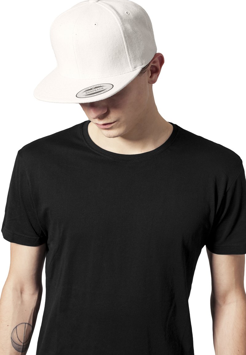 Fehér snapback sapka lapos karimával, gyapjú anyag; fekete rövid ujjú galléros pólóval párosítva. Minimalista dizájn, tiszta vonalak.