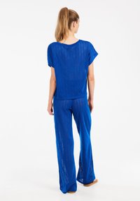 Blauwe gebreide top en losse broek met een open weefpatroon, met korte mouwen en wijde pijpen, gedragen door een persoon van achteren.