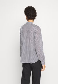 Blusa de manga larga con un patrón de corte de perro en blanco y negro, fabricada en un tejido ligero, con puños de botón y un dobladillo redondeado, combinada con pantalones negros.