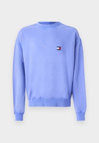 Sudadera de cuello redondo de color púrpura claro hecha de un tejido suave, con puños y dobladillo acanalados, que presenta un pequeño parche de logo en rojo, blanco y azul.