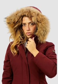 Cappotto invernale bordeaux con cappuccio foderato in pelliccia, dotato di chiusura con cerniera e colletto rialzato, con una texture liscia e leggermente lucida.