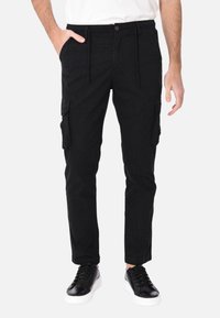 Pantaloni cargo neri in cotone con una vestibilità affusolata, dotati di tasche laterali e vita con cordoncino. Abbinati a scarpe da ginnastica nere.