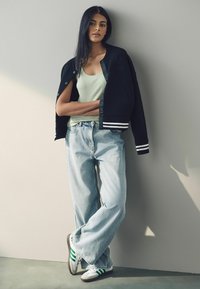 Černá varsity bunda se světlými pruhy, mintově zelený top na ramínka, světle modré baggy džíny a bílé tenisky se zelenými detaily.