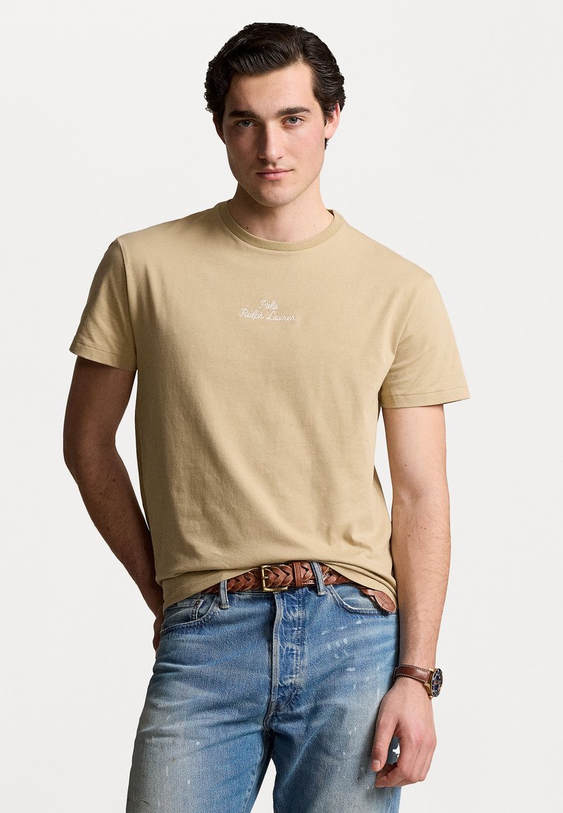 Tricou din bumbac bej, cu mâneci scurte, guler rotund și logo brodat. Purtați-l cu blugi de un albastru deschis și o curea împletită maro.