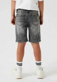 Shorts en jean noir délavé avec une finition usée, dotés de poches à patch et de ourlets retroussés. Portés avec des baskets blanches et des chaussettes rayées.