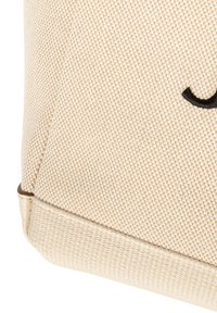 Płócienna torba w jasnym beżowym kolorze, z teksturowaną powierzchnią i czarnym haftowanym detalem. Zaokrąglone dno z przeszyciami.