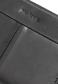 Black leather wallet featuring a textured surface, embossed "MAÎTRE" logo, and a zip closure. Includes two card slots and sleek design.