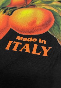 Schwarzer Stoff mit lebhaftem orangefarbenem Text "Hergestellt in ITALIEN" auf einem Hintergrund aus Orangenfrüchten und grünen Blättern.