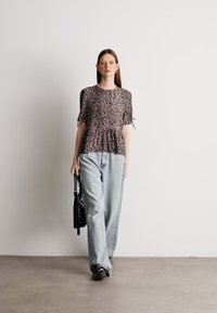 Ελαφρύ, κοντομάνικο τοπ σε σχέδιο λεοπάρ, συνδυασμένο με φαρδιά, ανοιχτό μπλε τζιν. Μαύρη τσάντα κρέμεται από το ένα χέρι.