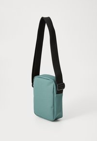 Small rectangular crossbody bag in textured teal fabric with a black adjustable strap and a plastic buckle, featuring clean lines and minimal design.