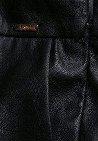 Tissu en cuir noir avec une surface texturée, présentant de subtiles creases et une étiquette de marque ton doré. Détail de fermeture éclair visible.