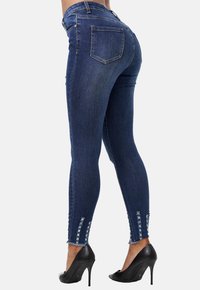 Jeans de mezclilla azul oscuro con un diseño ajustado, que presentan detalles rasgados en los dobladillos, combinados con zapatos de tacón alto negros.