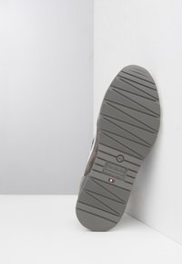 Suola in gomma grigia con battistrada testurizzato, dotata di logo e taglia. Parte superiore in suede mostrata in vista parziale, su uno sfondo chiaro.