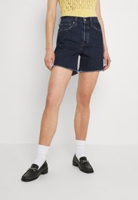 Jeansshorts i mörk tvätt med ruggad nederkant, femfickorsdesign och knappstängning. I kombination med svarta loafers och vita strumpor.