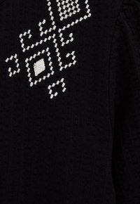 Sort tekstureret stof med hvide, broderede geometriske mønstre, herunder diamanter og firkanter, på den øverste sektion.