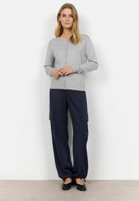 Cardigan grigio con bottoni, maniche lunghe e scollatura rotonda, abbinato a pantaloni cargo blu navy di taglio largo con tasche laterali. Scarpe nere flat.
