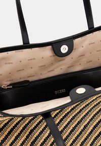 Zwarte en gouden geweven tas met een gestructureerd ontwerp, soepele zwarte handvatten en een beige interieur met een logo-patroon.