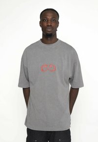 Szary, luźny t-shirt z krótkim rękawem i okrągłym dekoltem. Posiada centralny czerwony wzór graficzny. Miękka, teksturowana bawełniana tkanina.
